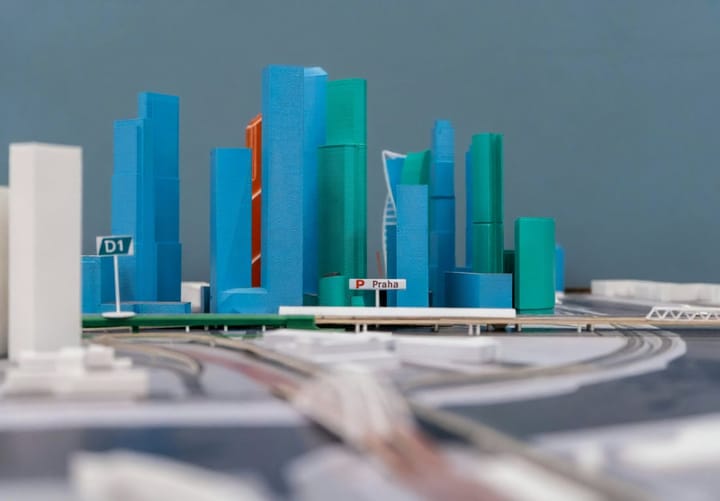 A close view of a 3D printed architectural model of a city, with tall buildings in blue and green and the road network between them. Labelled "Praha", it illustrates how 3D printing is used for detailed, realistic architectural visualisation.