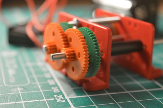 A close view of a 3D printed prototype of robotic parts, including red and green gears, laid out on a green cutting mat. It illustrates the production of components for robotics and automation.